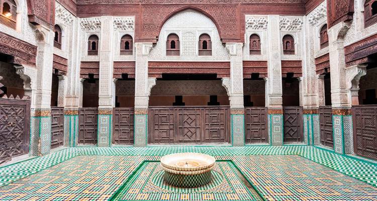 Makelloses Innenhof einer marokkanischen Madrasa mit komplizierten Zellige-Fliesen, geschnitztem Zedernholz und einem zentralen Brunnen