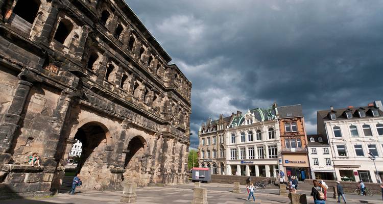 Monument historique en pierre avec des personnes se promenant autour, sur fond de ciel nuageux.