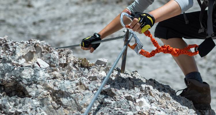 Climber securing themselves on a rocky trail with climbing equipment.