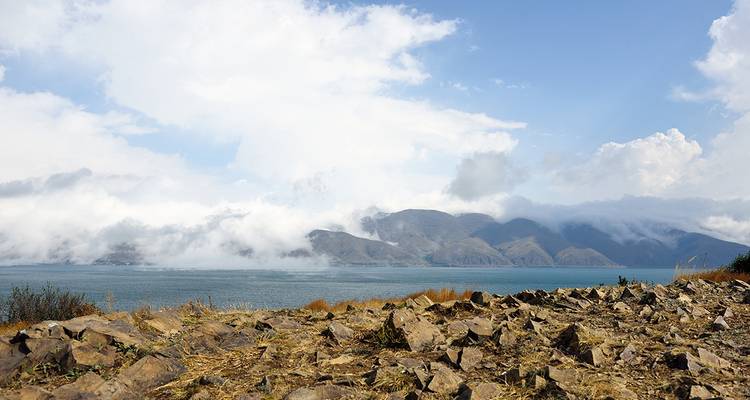See mit felsigem Ufer und Bergen in der Ferne.