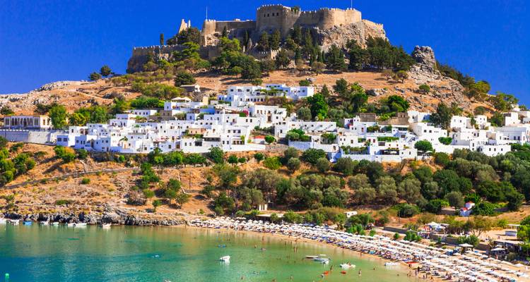 Pueblo encalado y antigua fortaleza en la cima de la colina con vista a una playa de arena y bahía turquesa en un día soleado y brillante.