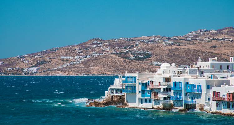 Maisons le long d'une zone côtière pittoresque avec des collines en arrière-plan.