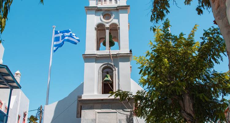 Tour d'église avec drapeau grec sous un ciel dégagé.