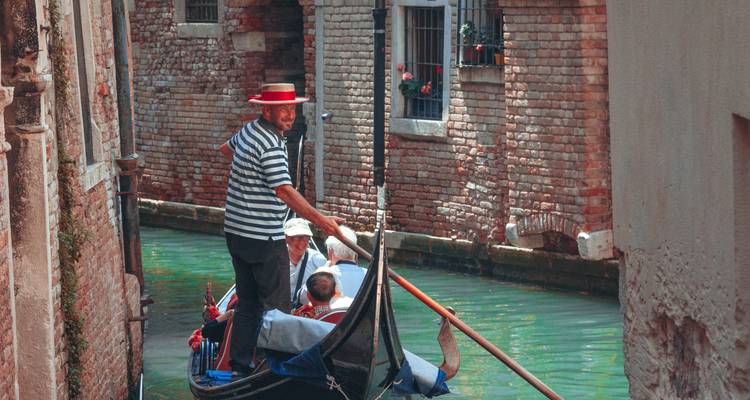 Gondolier dirigeant une gondole à travers un canal étroit.