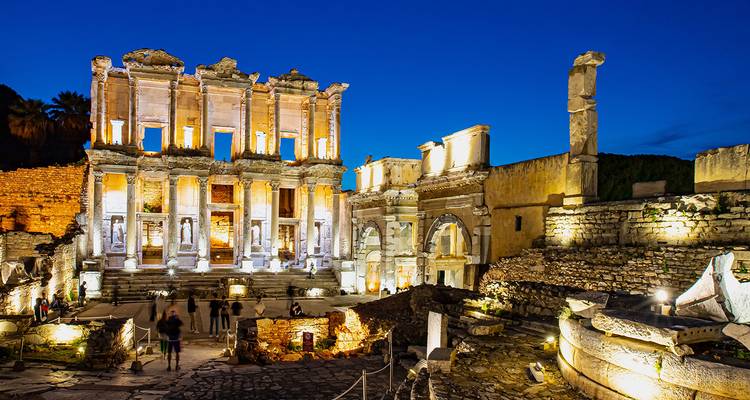 Ephesus Library illuminated at night with tourists exploring.