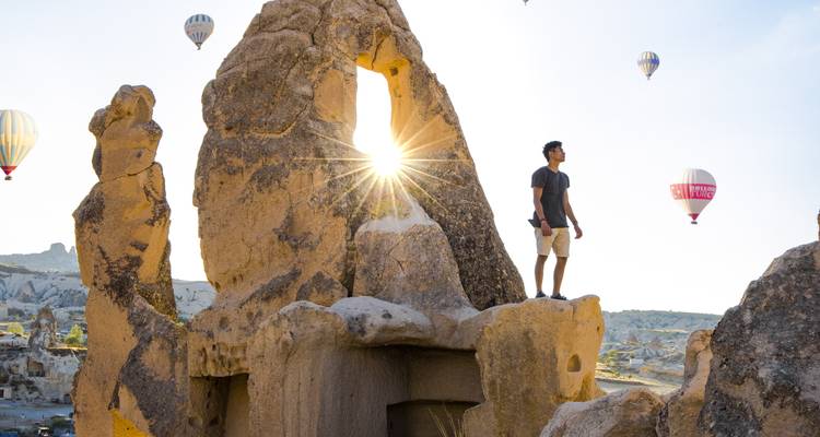Persona de pie sobre rocas con globos aerostáticos en el fondo.