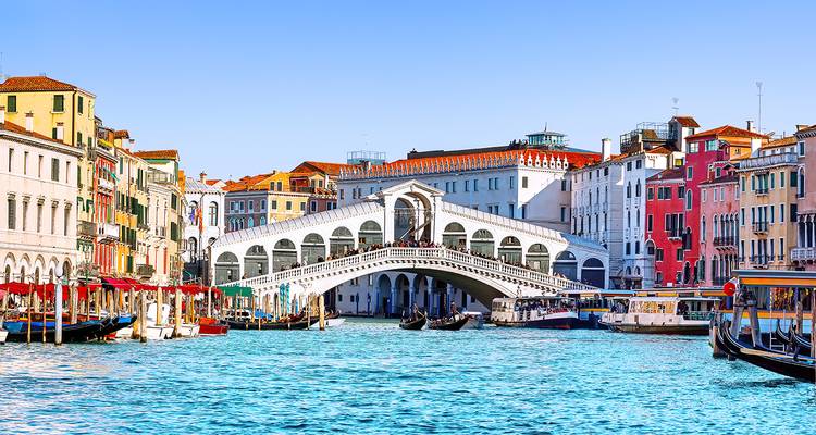 Pont emblématique du Rialto enjambant le Grand Canal à Venise avec des bâtiments historiques colorés et des gondoles par une journée claire et lumineuse