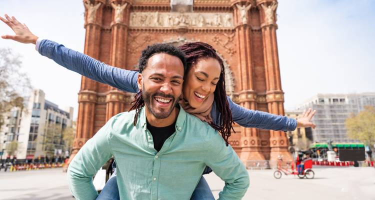 Pareja feliz posando frente a un gran arco de ladrillo in una ciudad.