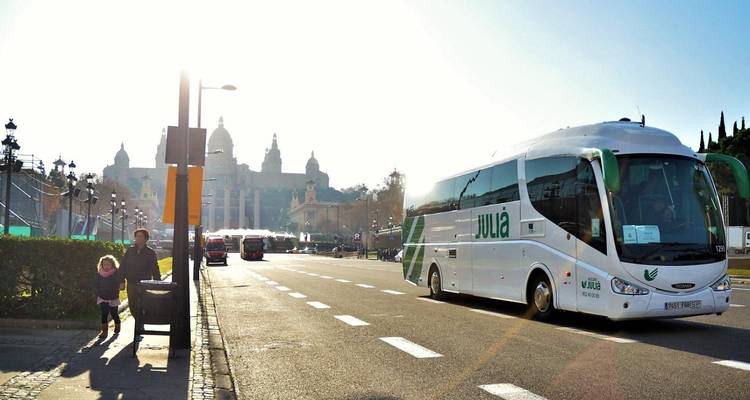 Un autocar touristique roulant sur un boulevard ensoleillé en direction du Palais National de Barcelone.