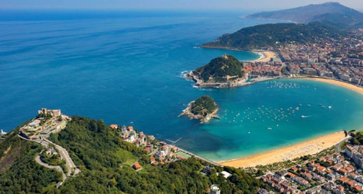Panorama aérien de la plage en croissant de Saint-Sébastien et de sa baie turquoise entourée de collines verdoyantes.