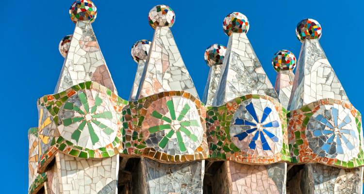 Cheminées colorées recouvertes de mosaïques au sommet de la Casa Batlló de Gaudí contre un ciel bleu clair.