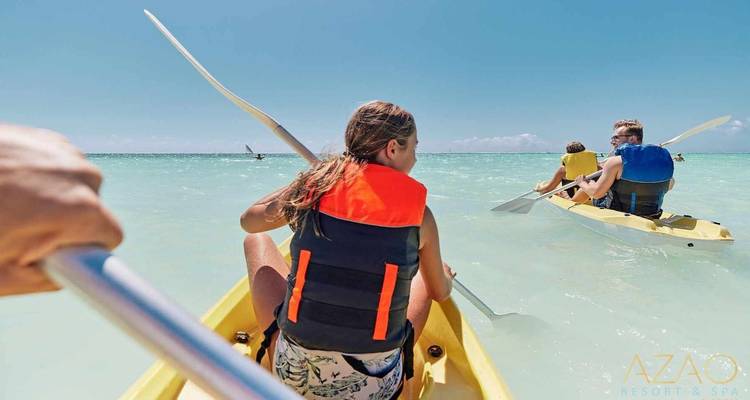 Personas haciendo kayak en aguas oceánicas cristalinas usando chalecos salvavidas.