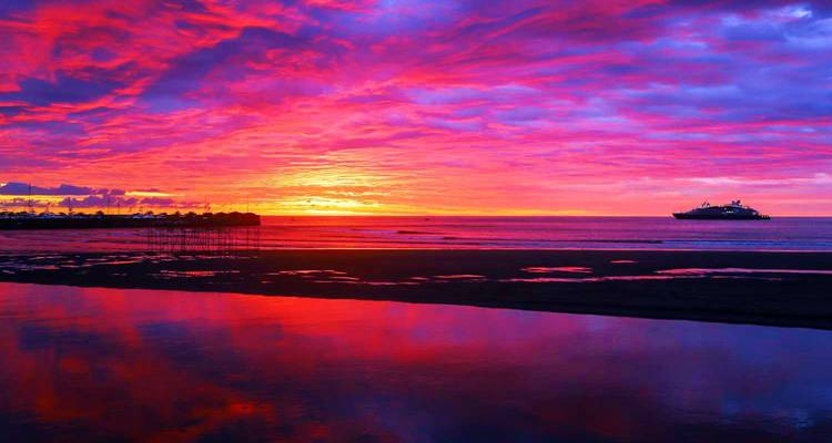 Levendige zonsondergang boven de oceaan met een schip aan de horizon.