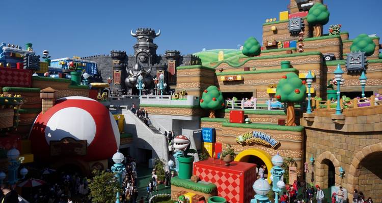 Parc d'attractions avec des bâtiments thématiques colorés et une foule.