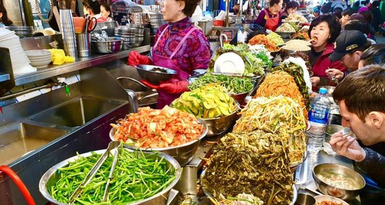Étal de marché alimentaire avec une variété de plats coréens traditionnels et des clients.