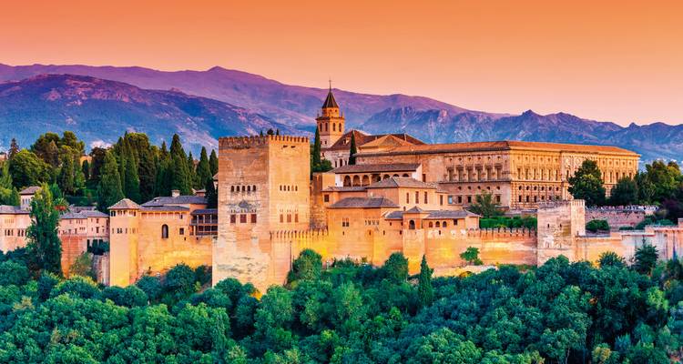 Der Alhambra-Palast bei Sonnenuntergang mit Bergen im Hintergrund.