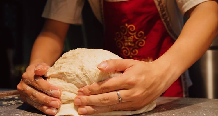 Hände kneten Brotteig auf einer Arbeitsplatte.