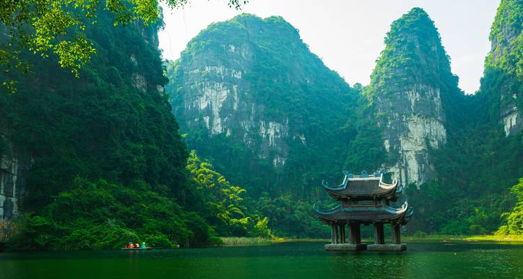 Pagode an einem ruhigen See, umrahmt von dramatischen Kalksteinfelsen.