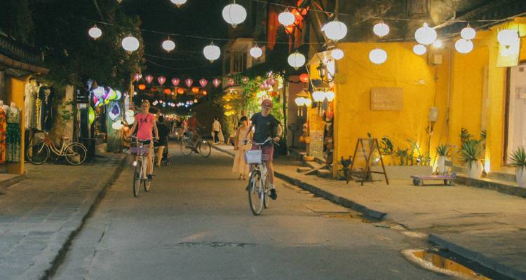 Menschen, die nachts auf einer mit Laternen geschmückten Straße Fahrrad fahren.
