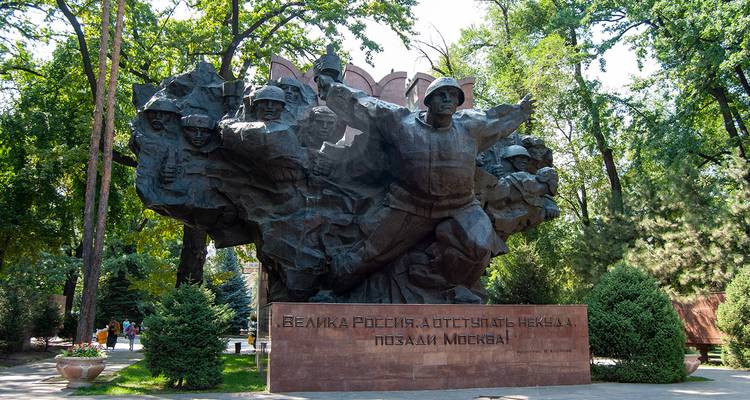 Un grand monument de guerre en bronze avec des soldats dans un cadre de parc.