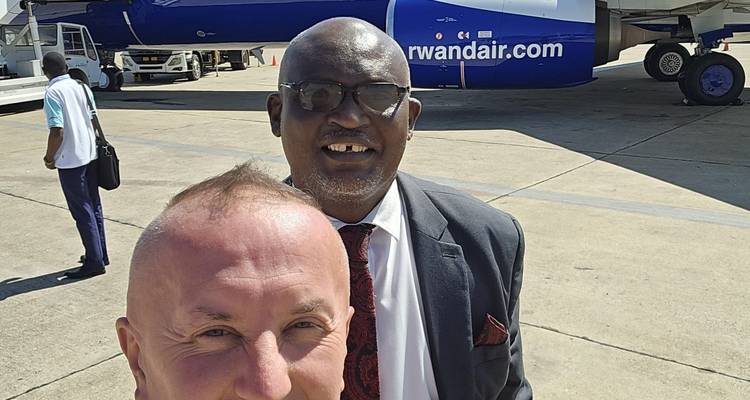 Deux hommes prenant un selfie sur un tarmac d'aéroport avec un avion en vue.