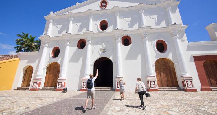 Trois personnes marchant vers une grande église de style colonial blanc.