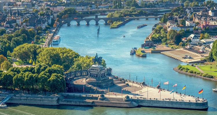 Panoramic aerial of Deutsches Eck monument where two rivers meet in Koblenz, with bridges and cityscape beyond.