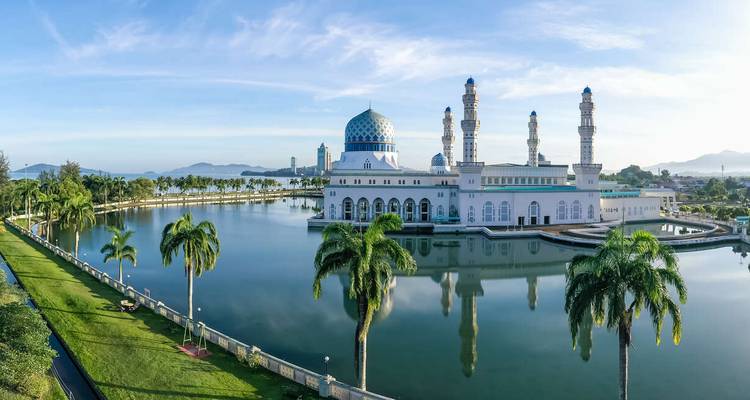Stunning mosque with blue dome set on a reflective lake surrounded by palm trees.
