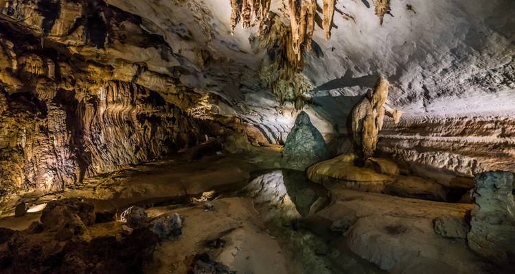 Intérieur de grotte spectaculaire avec stalactites reflétées dans un bassin peu profond.