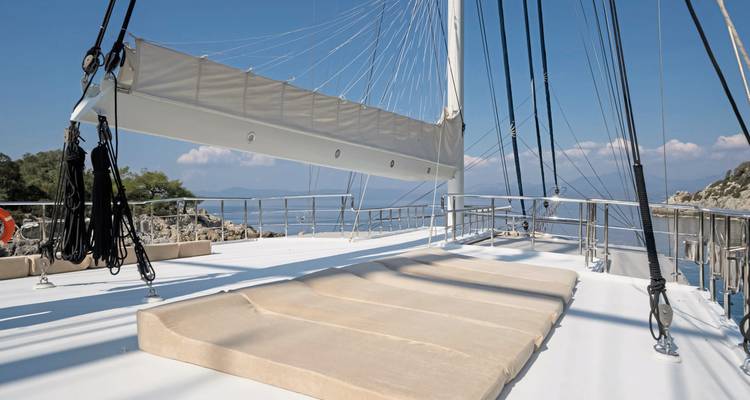 Dekzicht van een jacht overdag met een heldere hemel en kustlijn.