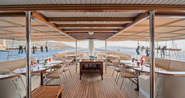 Ruime eetruimte op een boot met houten tafels en stoelen, met uitzicht op zee.