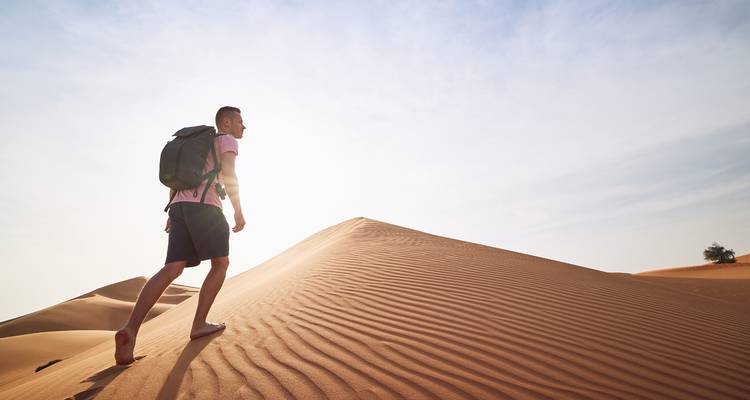 Man hiking on sand dunes with backpack under clear sky.