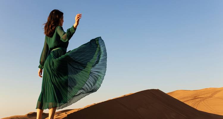Woman in green dress standing elegantly on sand dunes.