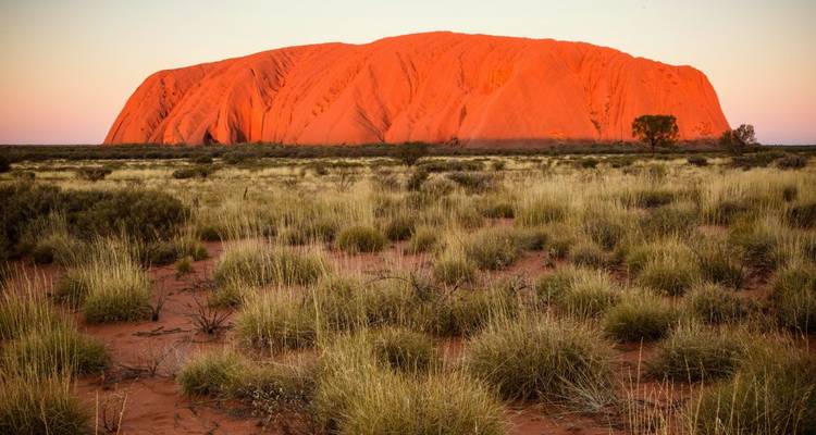 Uluru au coucher du soleil avec le rocher rouge qui domine le désert.