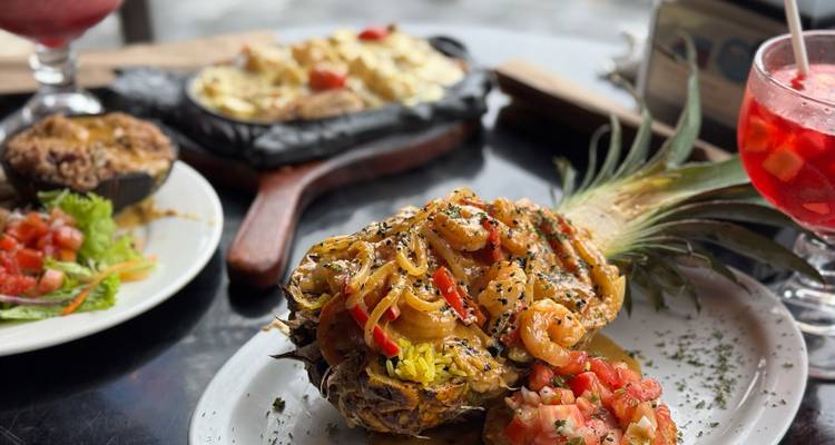 Tropical dish served in a pineapple with drinks on a table.