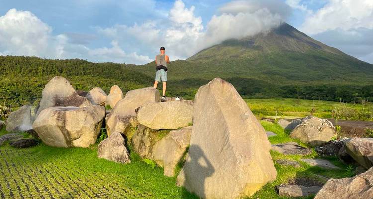 Hiker standing on rocks with a volcano in the background.
