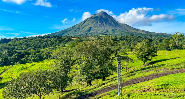 Volcán Arenal bajo un cielo azul despejado con vegetación circundante.