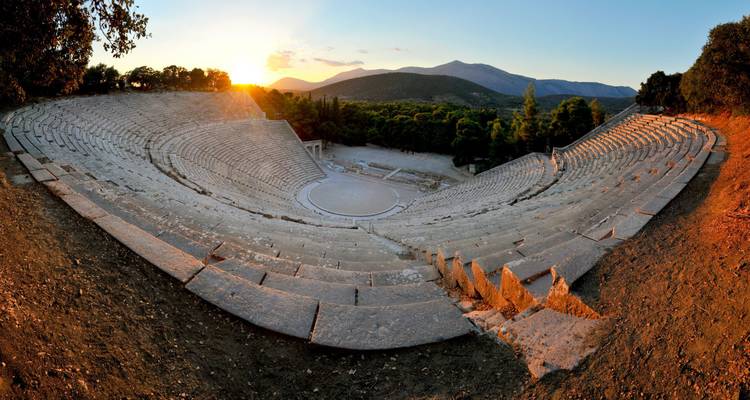 The ancient theater of Epidaurus with mountains in the background at sunset.
