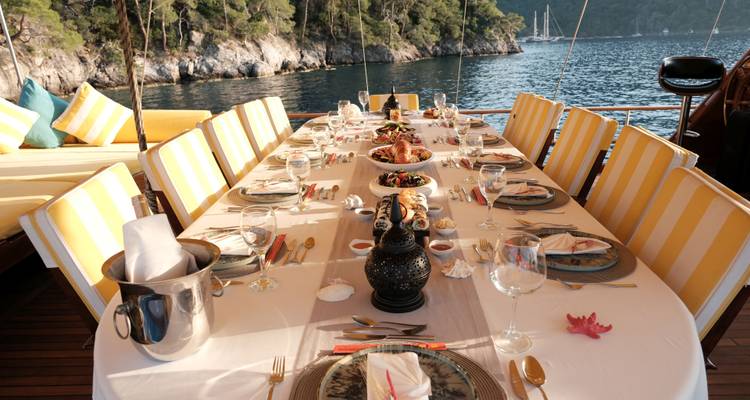 Une table de salle à manger joliment dressée sur une terrasse avec vue sur la mer et les îles.