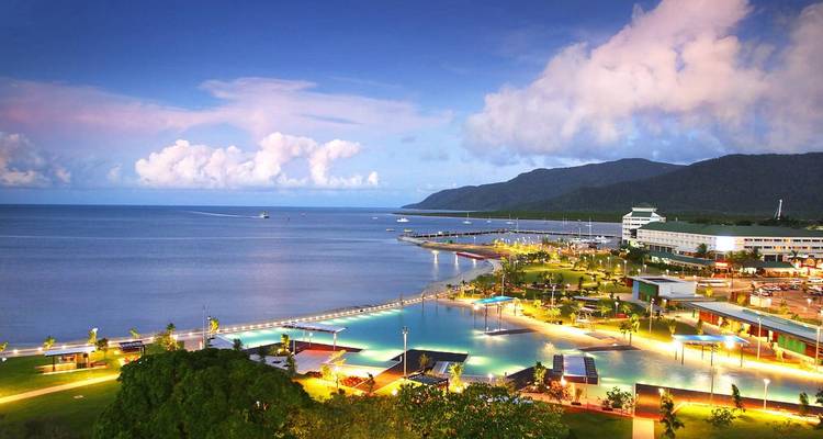 A modern coastal city with a vibrant waterfront lit up at night.