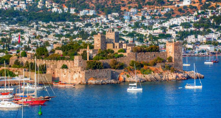 Château avec yachts dans le port devant un paysage urbain.