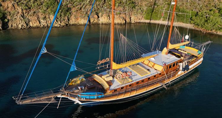 Vue aérienne d'un grand yacht à voiles ancré dans une baie aux eaux bleues cristallines.