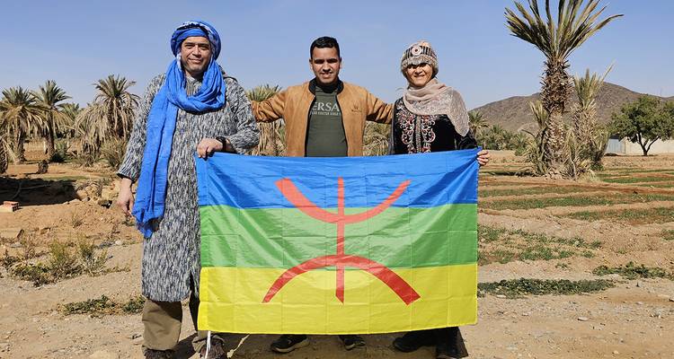 Three people with a colorful flag in a desert setting.
