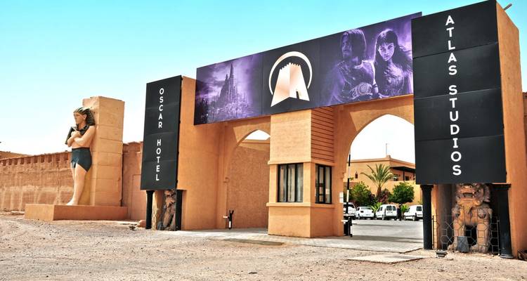 Puerta de entrada a Atlas Studios con grandes carteles de películas y una estatua monumental contra un cielo azul claro del desierto.