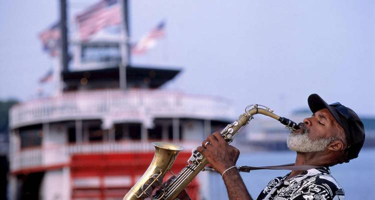 Homme jouant du saxophone avec un bateau fluvial en arrière-plan.