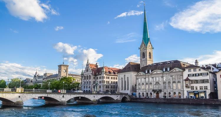 Vue pittoresque d'une rivière avec un pont et des bâtiments historiques, mettant en vedette un clocher d'église imposant.