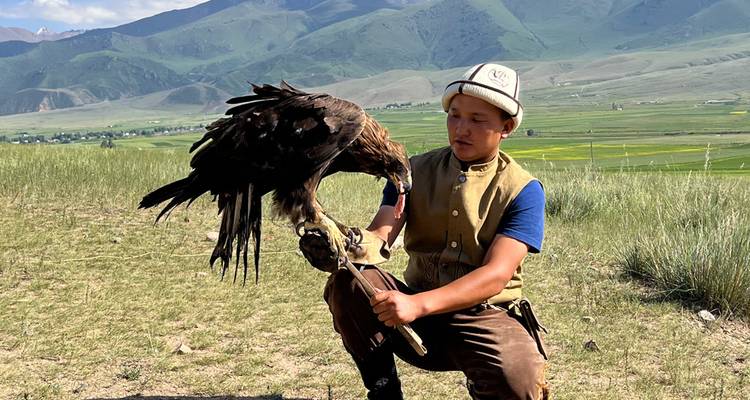 Jongere die een arend vasthoudt in een bergachtig landschap.
