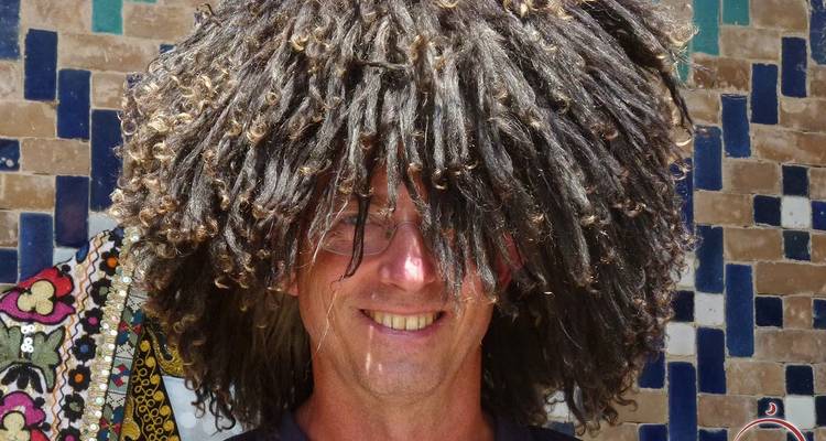 Personne avec une grande coiffe décorative devant un mur à motifs.