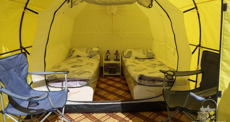 Vue intérieure d'une tente de camping avec deux lits et des chaises.