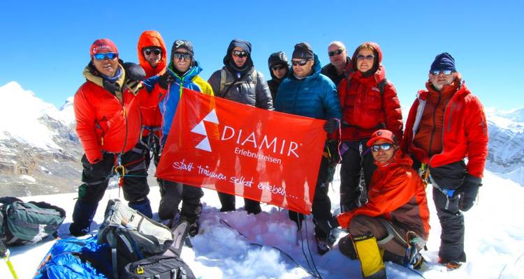 Grupo de escaladores posando con una bandera en una cima nevada.